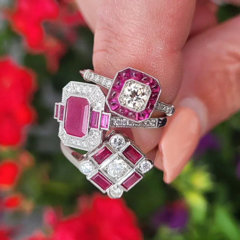 Three Art Deco ruby and diamond rings held in a hand against flowers